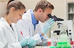 Two happy students looking through microscope and taking notes in lab at college