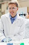 Smiling handsome student in lab coat looking at camera in lab at college