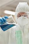 Lab assistant with mask pouring blue liquid in beaker in lab at college