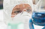 Lab assistant with mask looking closely at blue liquid in lab at college