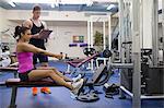 Instructor taking notes of woman exercising in weights room of gym