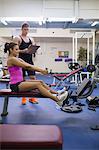 Instructor taking notes of sporty woman exercising in weights room of gym