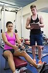 Instructor taking notes of toned brunette exercising in weights room of gym