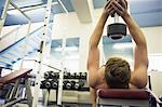 Muscular man holding heavy dumbbell over head in weights room of gym