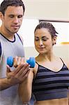 Instructor assisting content brunette lifting dumbbells in weights room of gym