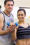 Instructor assisting smiling brunette lifting dumbbells in weights room of gym