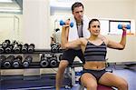 Trainer correcting sporty brunette lifting dumbbells in weights room of gym