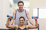 Trainer correcting cheerful woman lifting dumbbells in weights room of gym