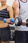 Attractive woman and man lifting dumbbells in weights room of gym