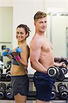 Smiling man and woman holding dumbbells in weights room of gym