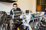 Happy repairman standing behind an engine in workshop