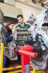 Concentrating trainee and instructor repairing an engine in workshop