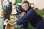 Smiling trainee with safety glasses drilling wood in workshop
