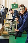 Cheerful trainee with safety glasses drilling wood in workshop
