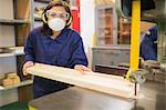Apprentice wearing safety protection using saw in workshop