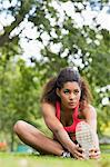 Beautiful sporty young woman stretching her leg while sitting in the park