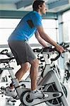 Side view of a smiling young man working out at spinning class in gym