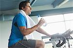 Side view of a tired young man with water bottle working out at spinning class in gym