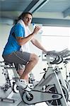 Side view portrait of a tired young man with water bottle working out at spinning class in gym