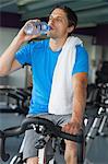 Tired young man drinking water while working out at spinning class in gym