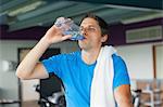 Tired young man drinking water while working out in the gym