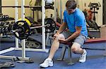 Full length of a healthy young man with an injured leg sitting in the gym