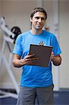 Portrait of a smiling trainer with clipboard standing in the gym