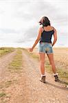 Full length rear view of a cool young woman hitchhiking on dirt countryside road
