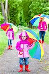 mother and her daughters with umbrellas in spring alley