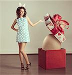 very cute young woman in spring ligh blue dress, with easter bunny ears ,near a big box with egg inside