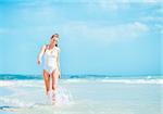 Young woman in swimsuit walking on sea shore