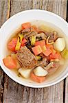 Rustic Beef Soup with Potato, Carrot, Leek and Greens in White Bowl closeup on Wooden background. Top View