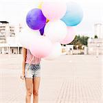 girl in short jeans shorts, sleeveless striped top and high heels stands in bunch of balloons
