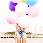 close-up of girl in polka-dot short jeans shorts, sleeveless striped top hides in bunch of balloons