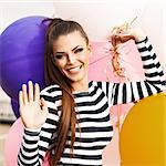 close-up of smiling girl with smokey eye make up and long hair in black and white striped dress waves holding bunch of multicolored balloons