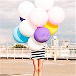 girl in black and white striped short dress and white high top sneakers hides in bunch of multicolored balloons