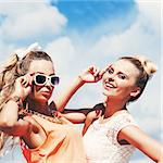 two young girls in summer outfit pose for the camera against the blue sky