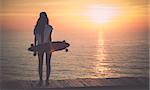 Beautiful girl with a skateboard looking to the sunset