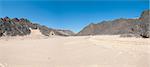 View down a dry wadi desert river valley in barren arid climate with mountains