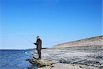 Man fishing at a flat rock coast at blue sky and blue water. From the swedish island Oland in Sweden.