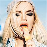 Portrait of beautiful blond girl with closed eyes and smokey eye makeup who enjoys licking ice cream with her tongue