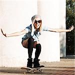 Beautiful smiling blond girl in sunglasses, shorts and stockings rides happily on skateboard