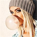Close-up of beautiful young blond girl in beanie hat blows big bubble from bubble gum