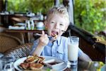 little boy having his breakfast with pancakes and milk at the resort during vacation