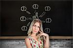 Frowning pretty blonde wearing flowered dress posing against chalkboard on grey brick wall