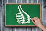 Composite image of hand drawing thumbs up with chalk on chalkboard on grey wooden planks