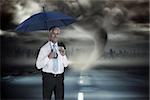 Happy businessman holding umbrella against stormy sky with tornado over road