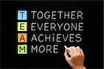 Hand writing TEAM - Together Everyone Achieves More with white chalk on blackboard.