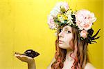 calm pretty girl with snail in hand and flower crown on head on yellow background