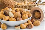 pistachio, peanuts, almonds, hazelnuts, walnuts, brazil nuts, coconut and wooden nut cracker on small bowl in front of basket